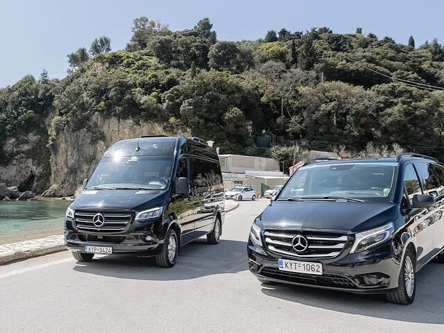 Two black Mercedes vans parked on a road near a beach and hillside