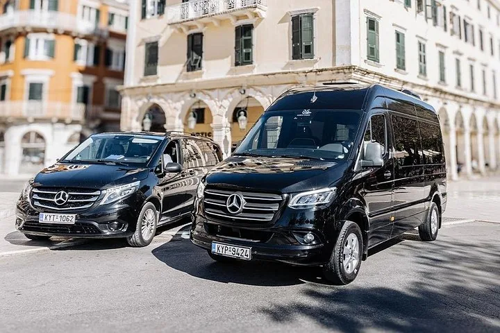 Two black Mercedes passenger vans parked on a paved street in front of a building