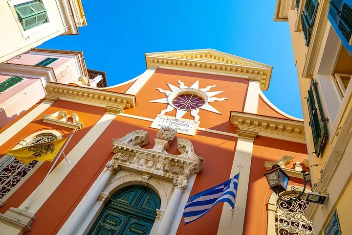 Low angle view of an orange church facade with Greek flag and sunny sky