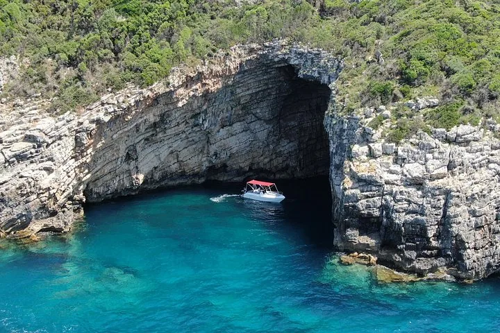 Small white boat entering a large sea cave carved into a rugged cliff
